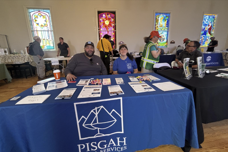 Two people staffing a resource table with a blue table cloth and stacks of handouts