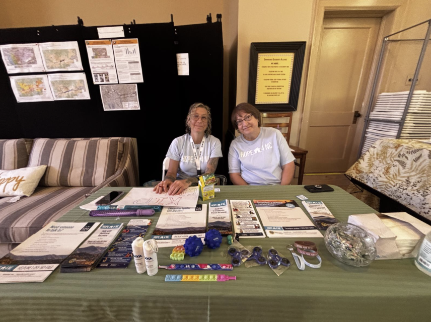 Two volunteers staff a resource table with handouts and swag