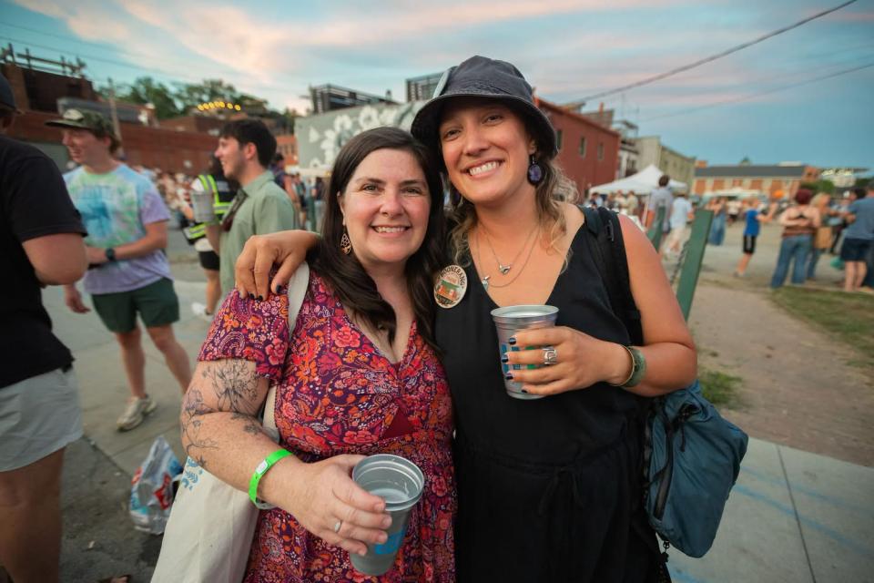Two women holding drinks pose for a photo in a downtown setting