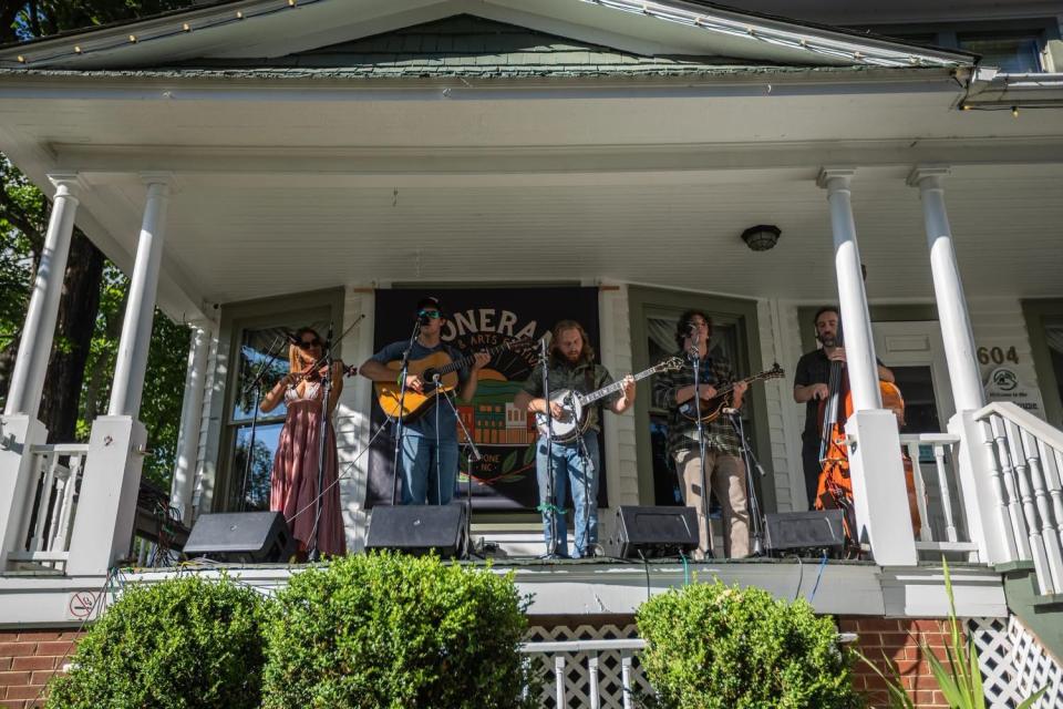Five people play stringed instruments from a porch