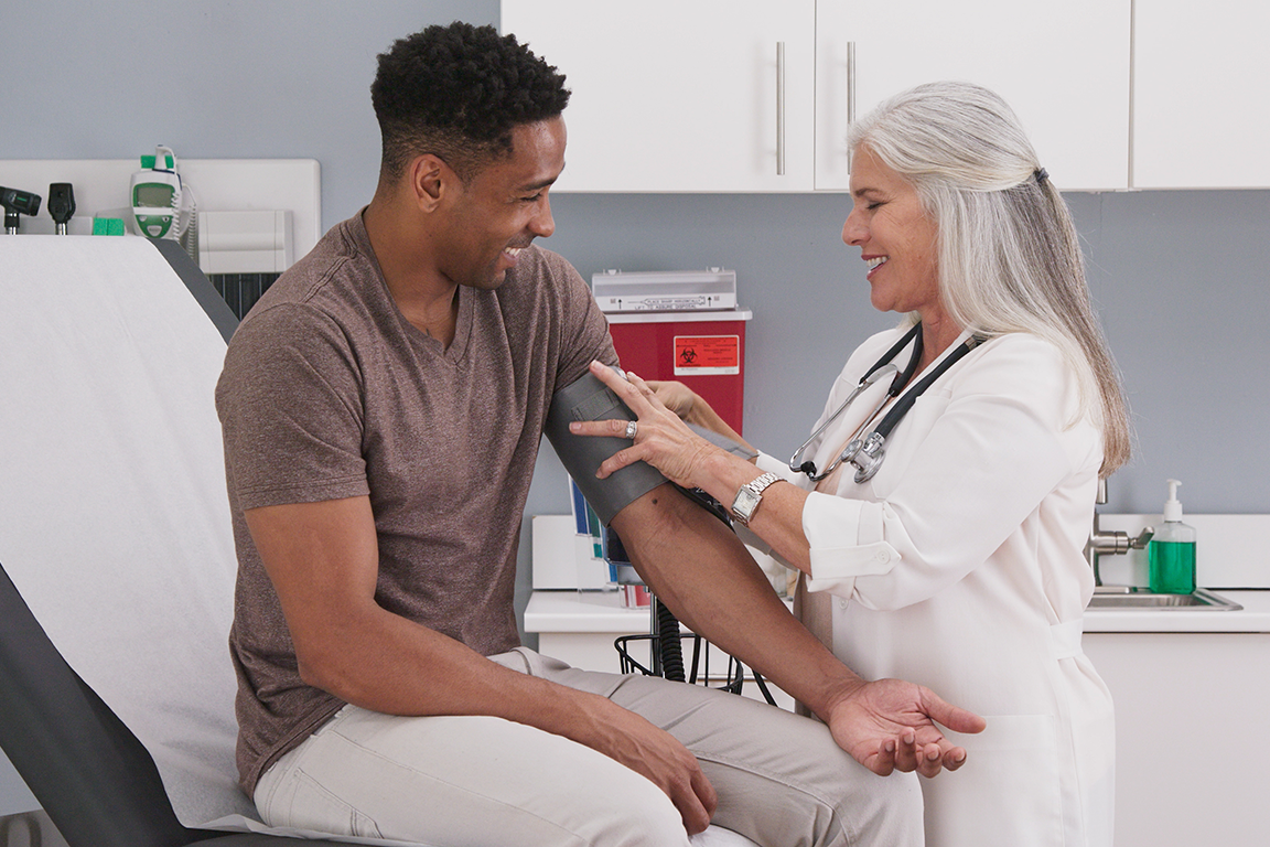 A young black man having his blood pressure checked by a female physician.