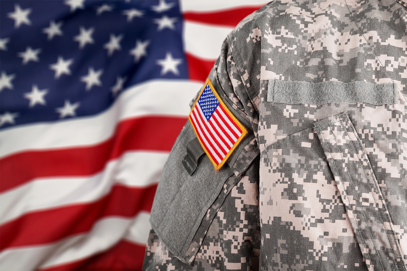 American soldier shoulder with United States flag patch and an American flag in the background.