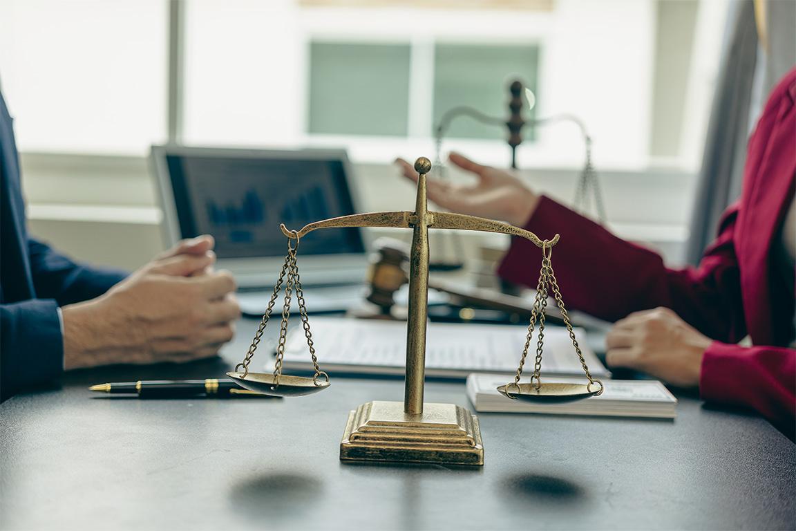 A lawyer sharing legal advice with a client at a desk with a legal scale in foreground.