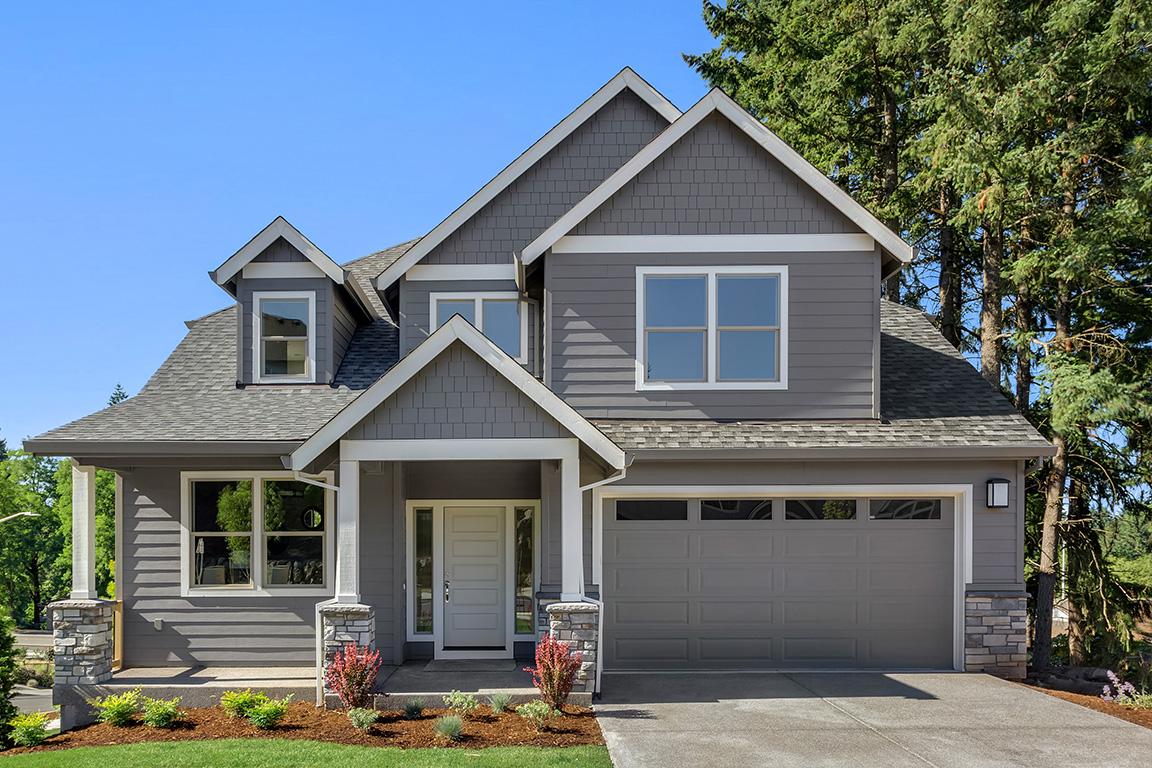 A grey sided, two-story single family home with garage and trees.