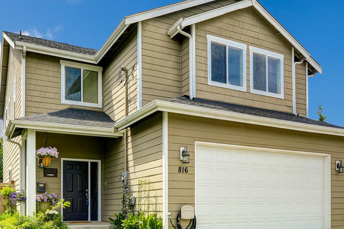 A tan, two-story house with garage on a sunny day.
