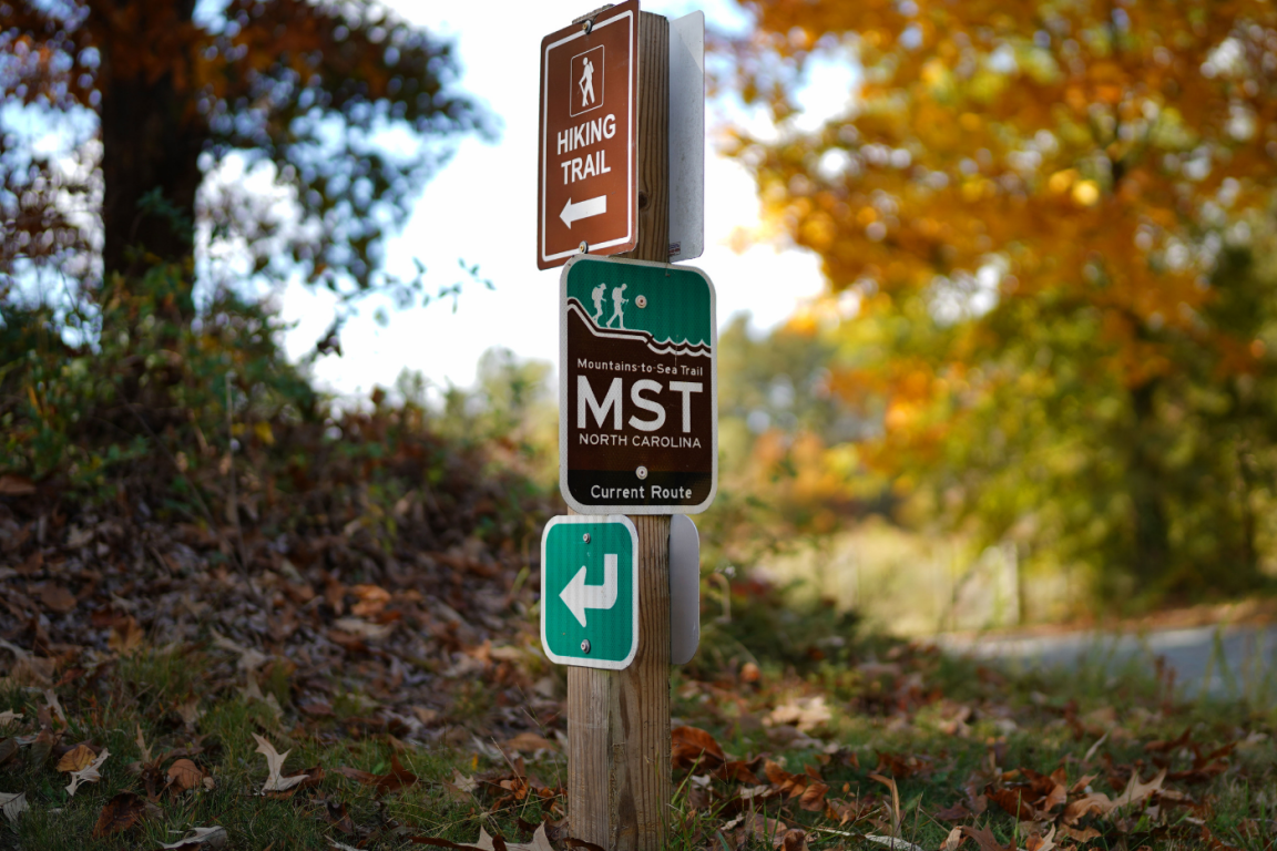 A sign post on a wooded trail showing directions to hiking trail.