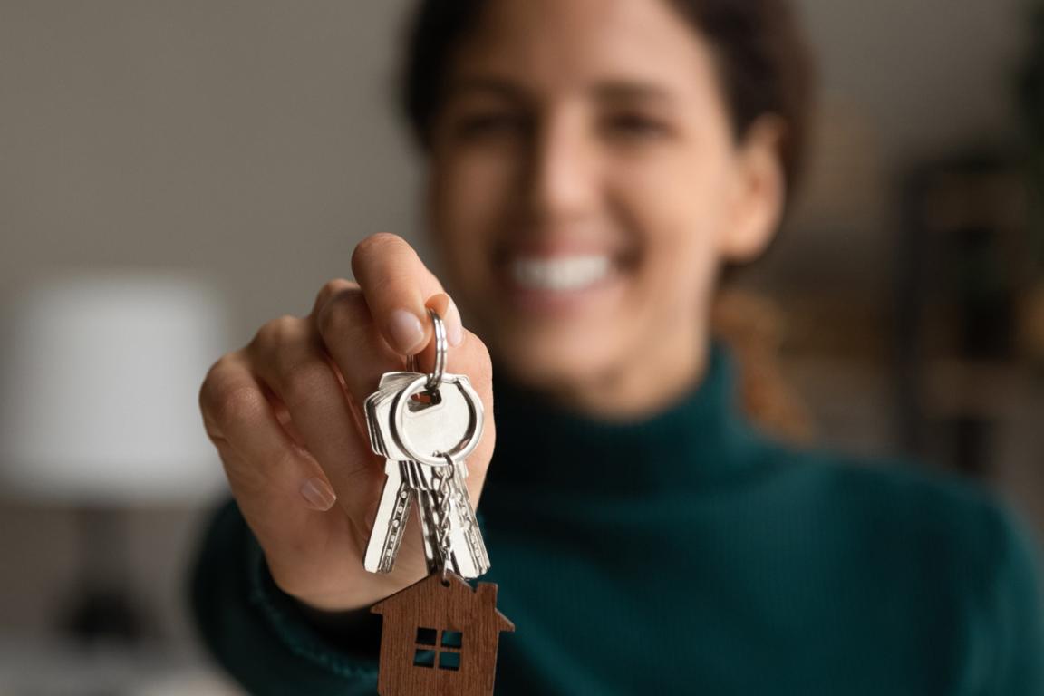 A young, smiling woman holding the keys to her new home.