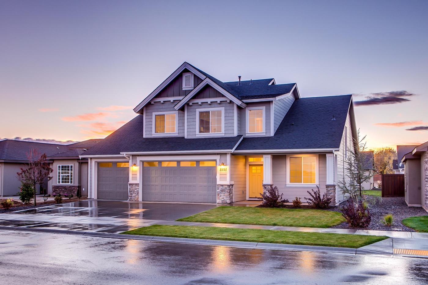 Two story house with blue and light gray siding on with yellow glow of lights in windows.