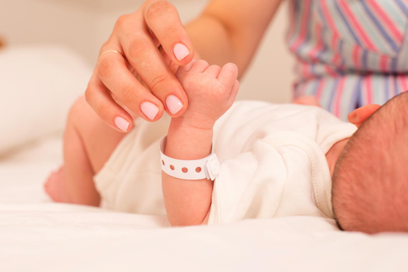 Lying infant with hospital bracelet holding mother's hand.