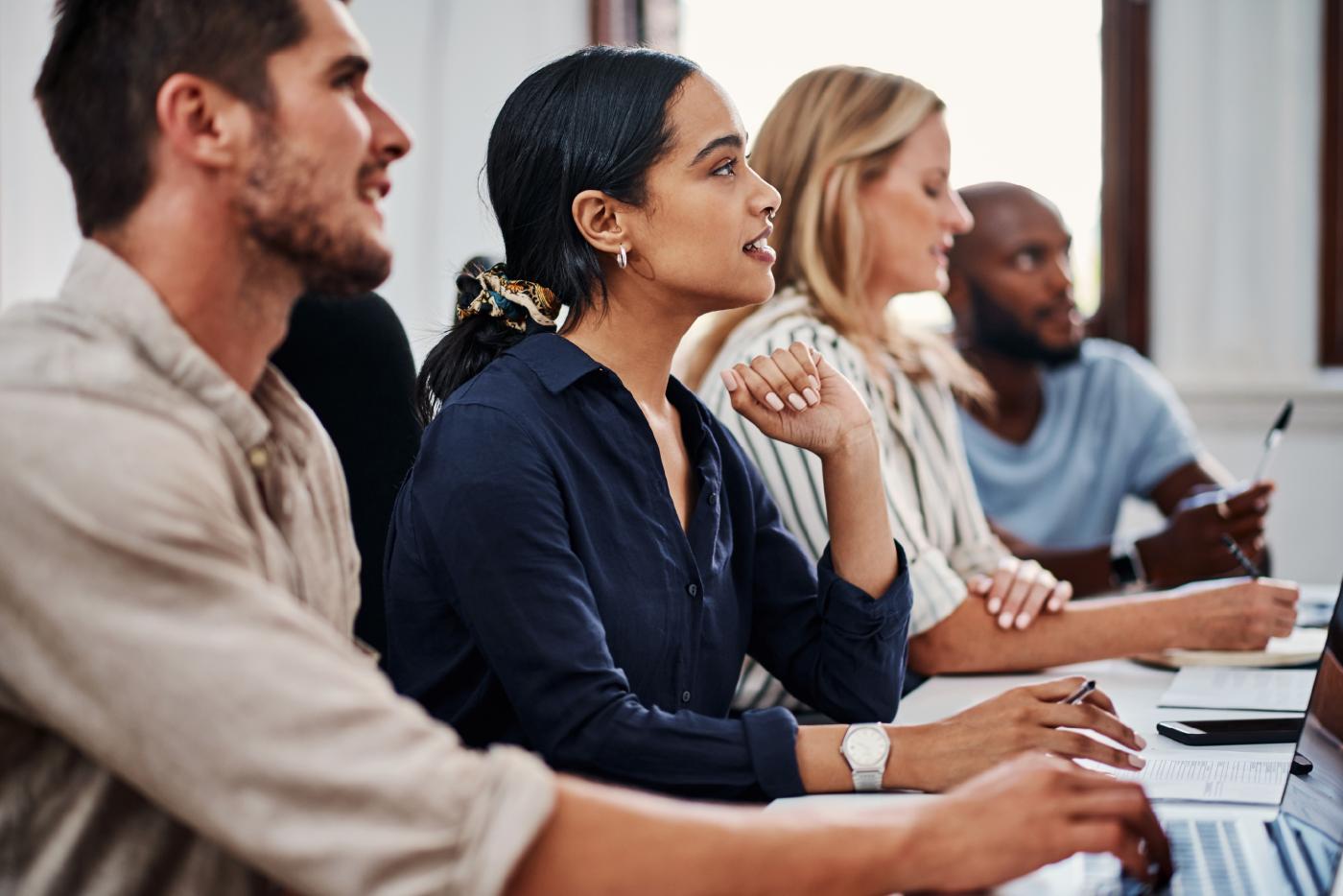 Attendees with laptops at a meeting listening attentively to the presenter.