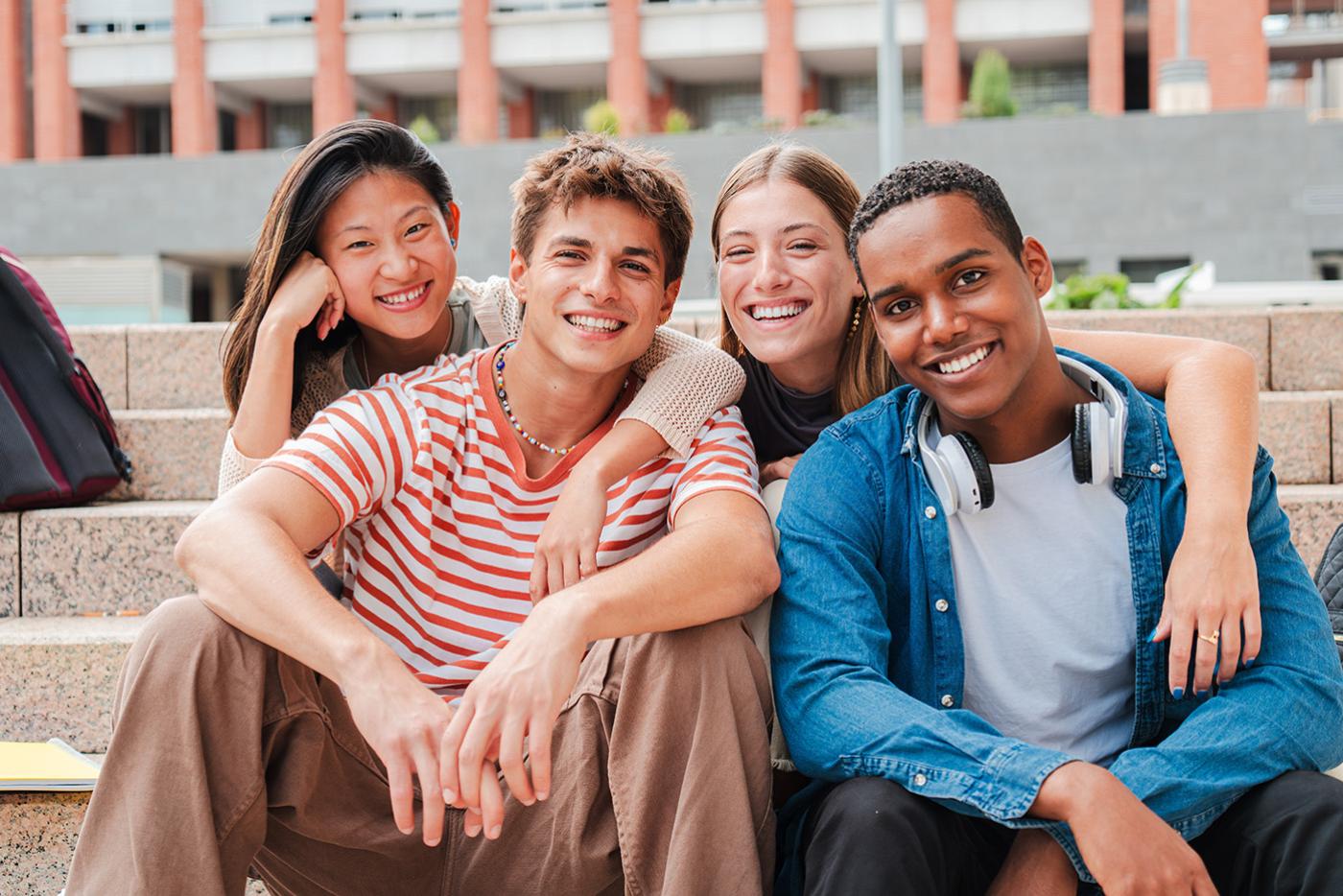 Group of smiling high school students seated outside on school steps.