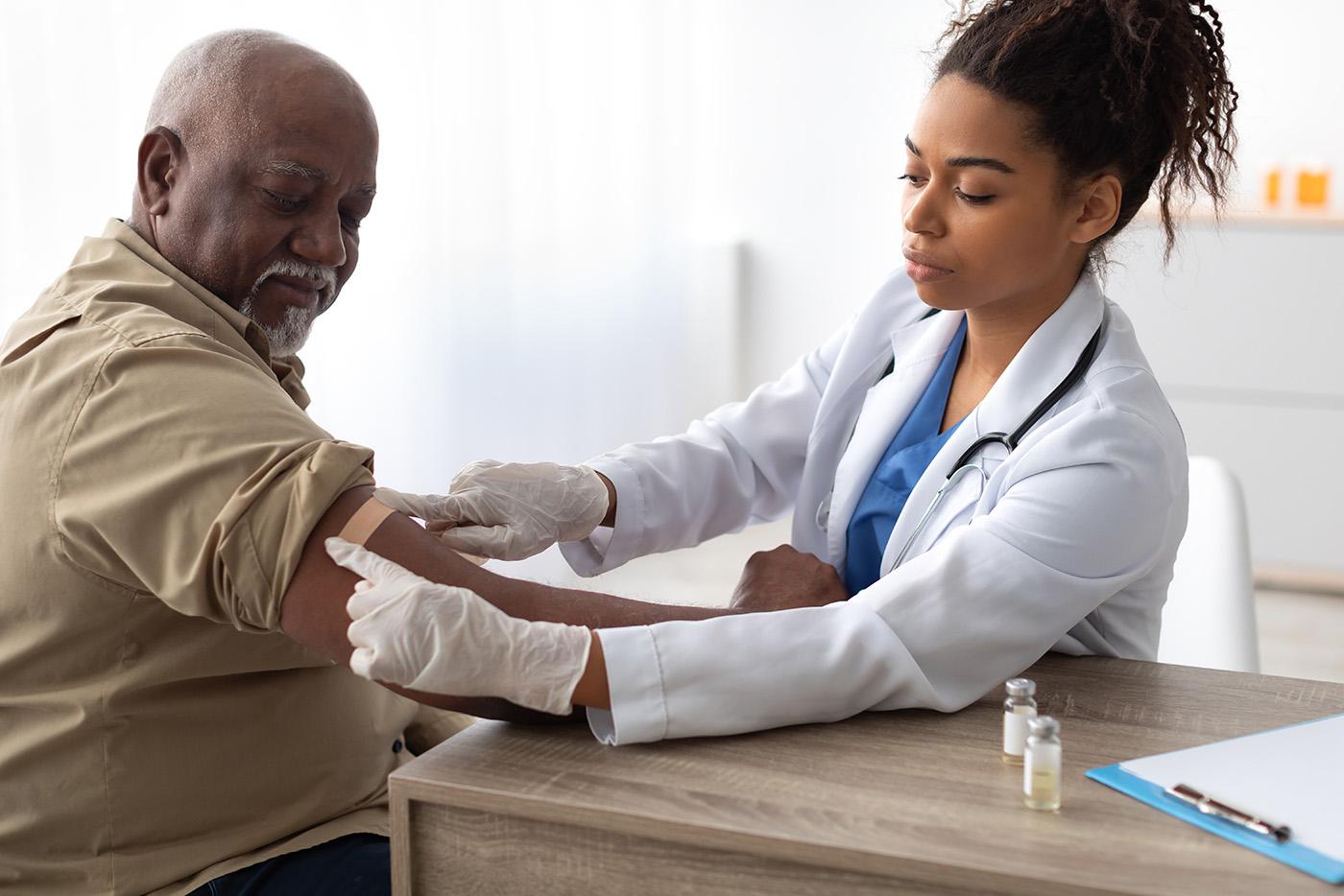 Female doctor applies band aid to elderly man's arm after receiving seasonal flu vaccine.