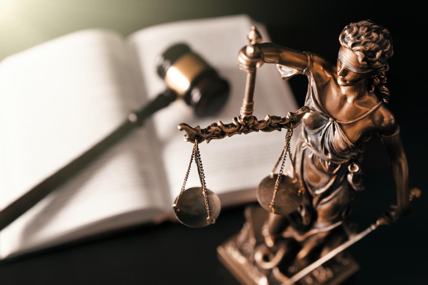 Statue of lady liberty on a desk with a gavel in the background.
