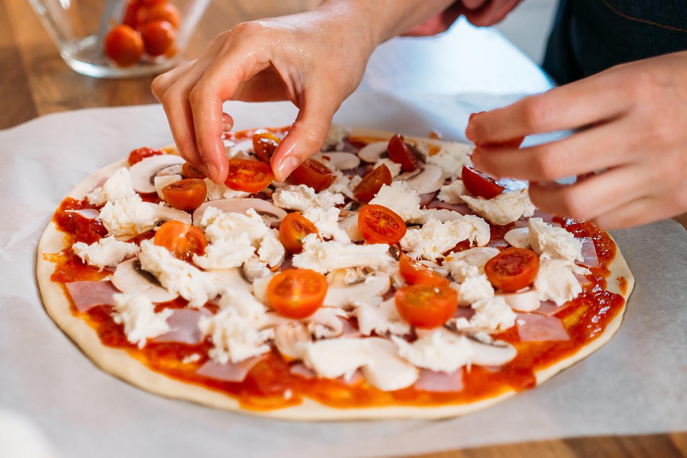 Woman's hands adding cherry tomatoes to a traditional margarita pizza.