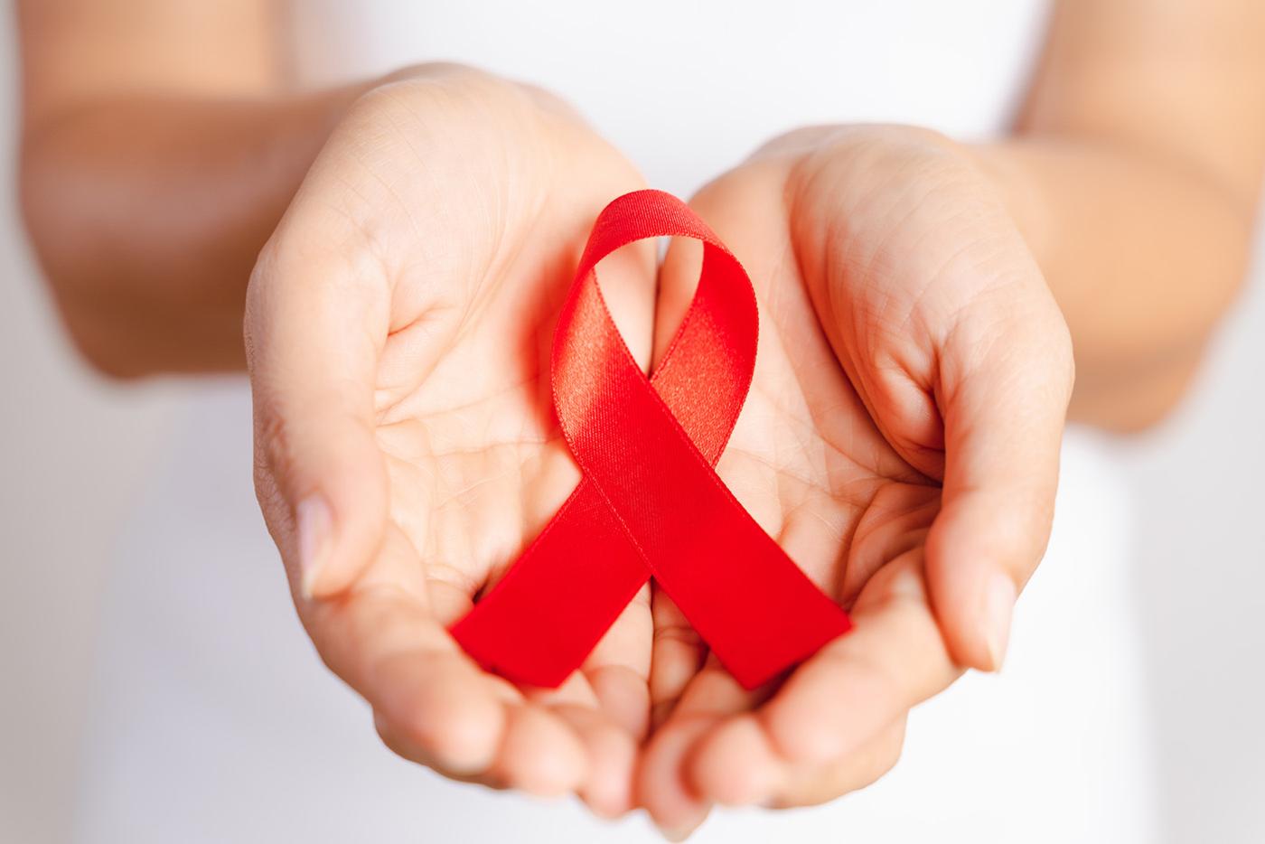 A woman's open hands placed together and holding a red AIDS memorial ribbon.