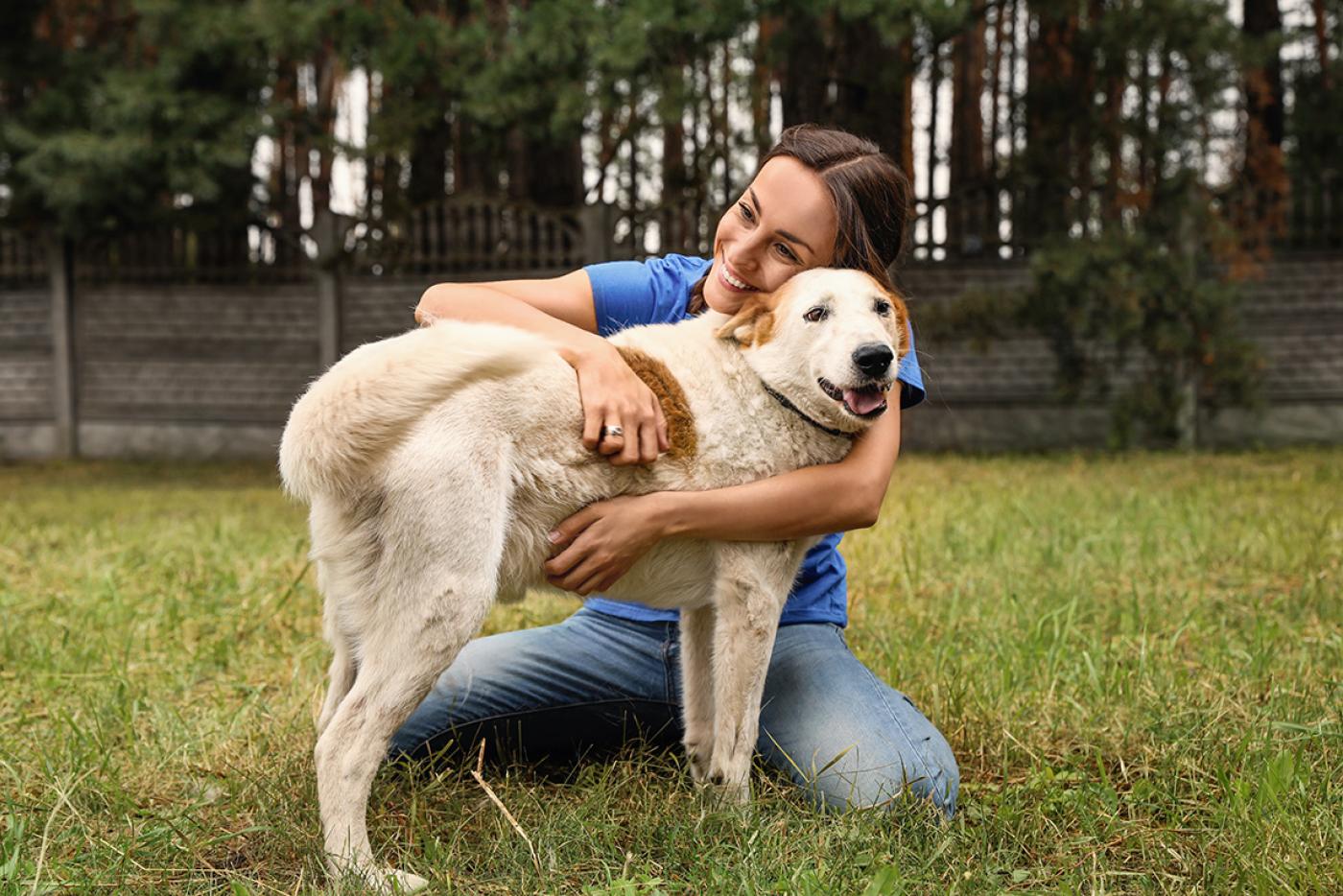 Caregiver at animal shelter kneeling and hugging light tan, medium sized dog.