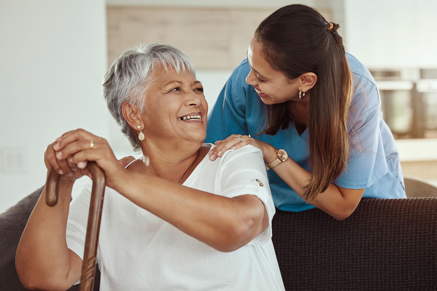 A senior woman seated with cane, smiling at a female care giver.