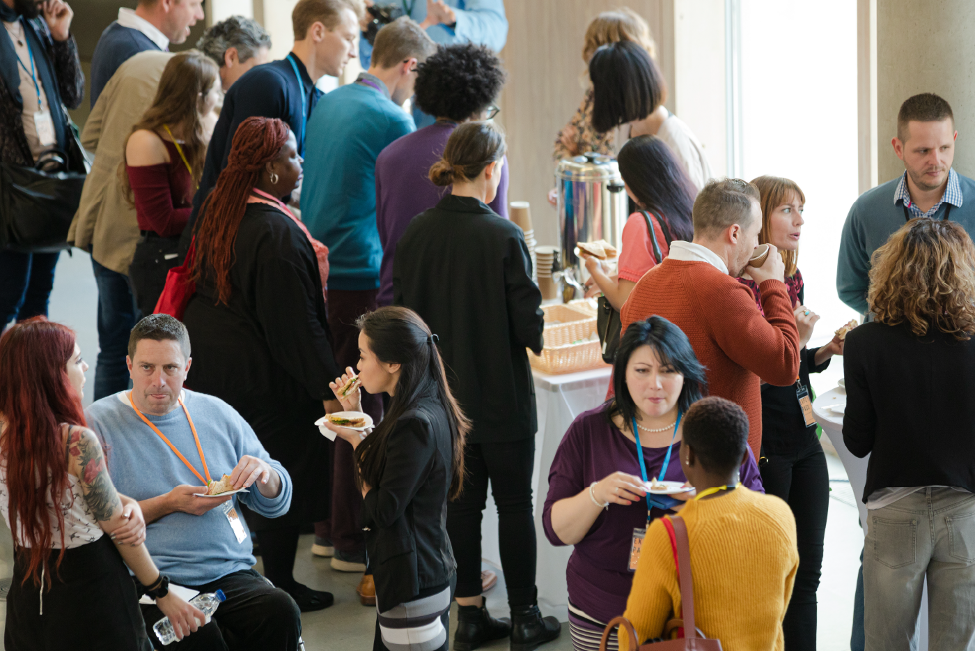 A diverse group of people at a conference event sharing food, drinks, and conversation.