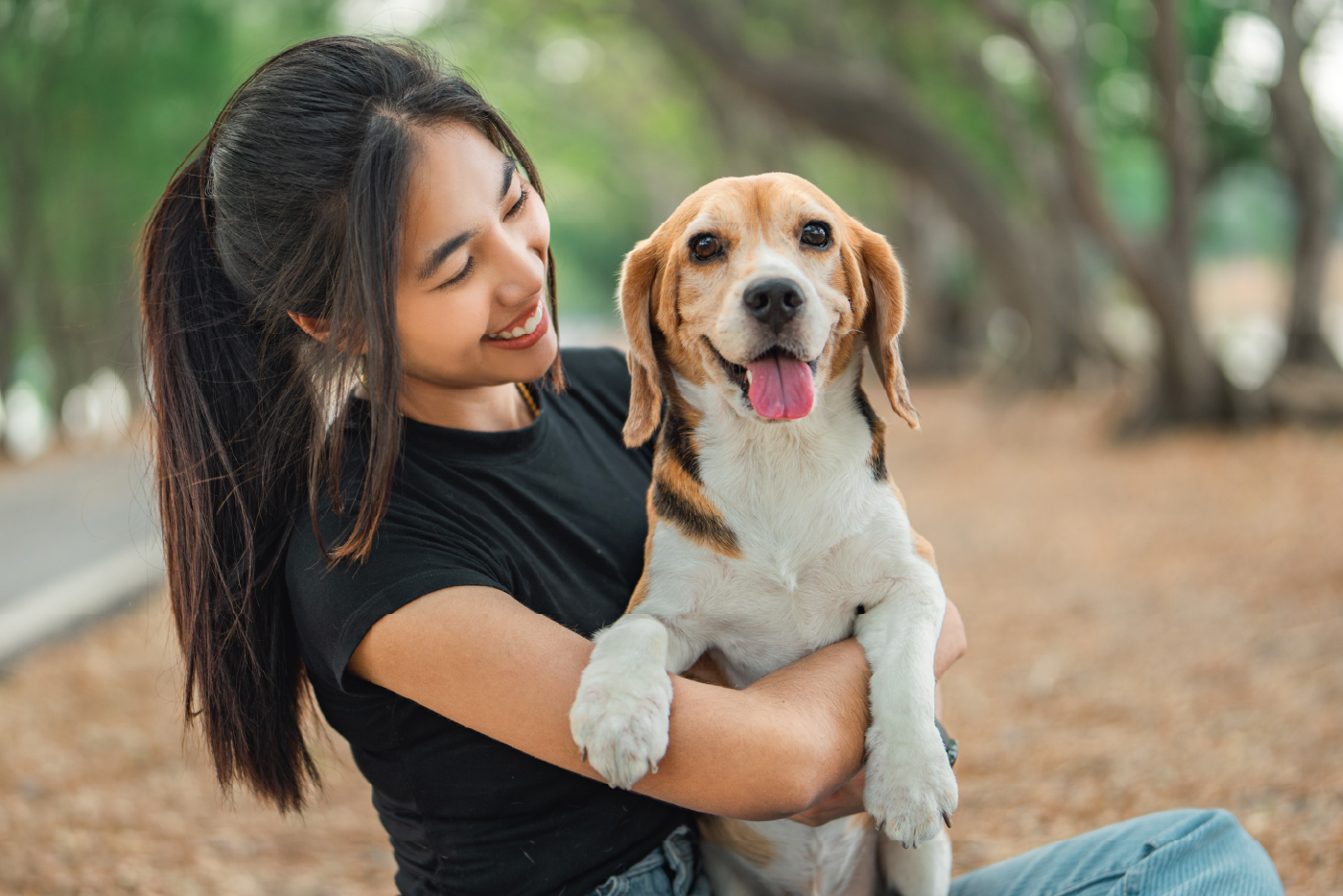 Smiling young woman holding her white, tan, and black beagle.