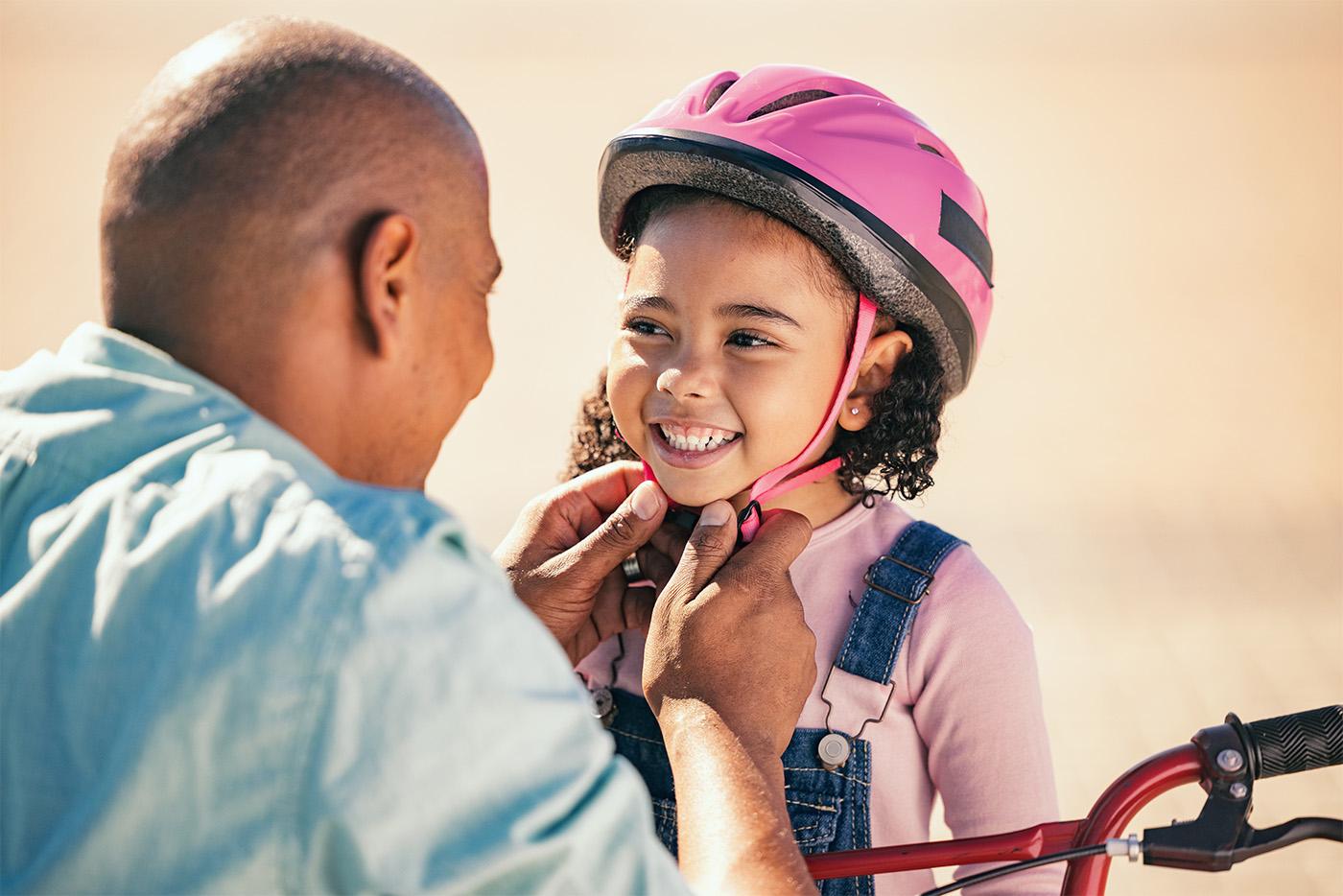 A father secures a pink bicycle helmet on his young daughter before a bike ride.