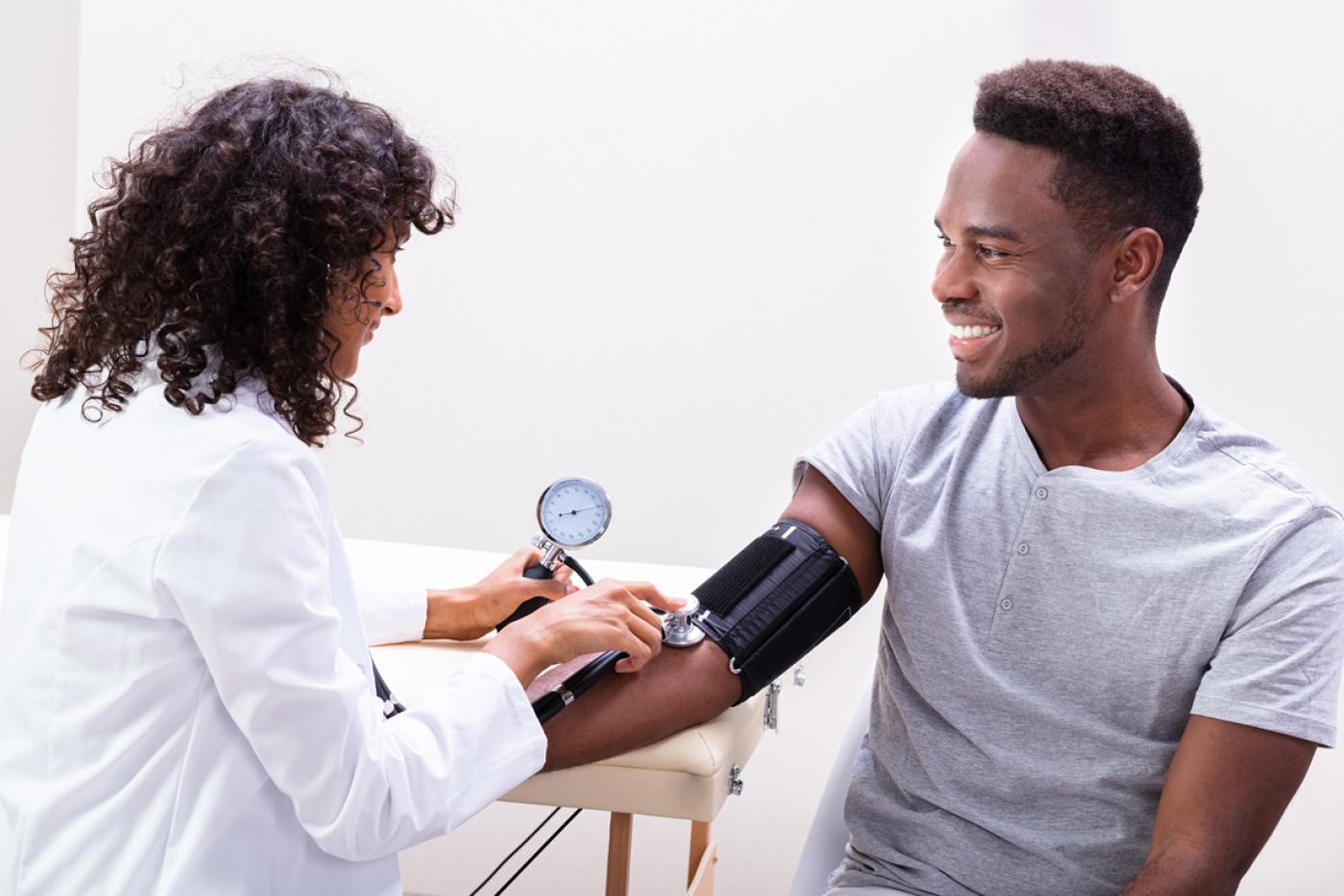 A young black man having his blood pressure checked by a female physician.