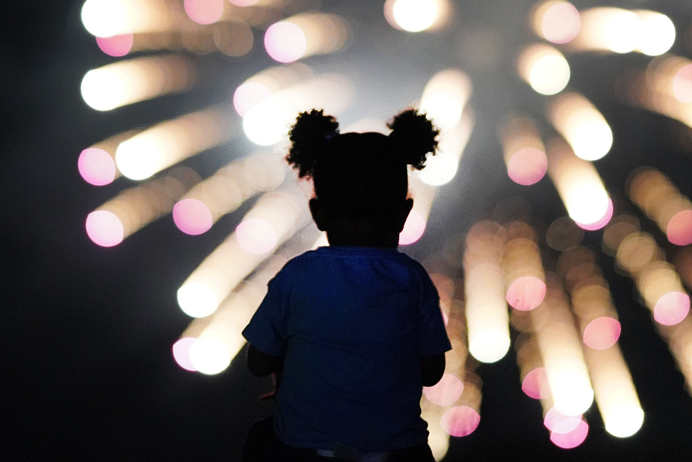 Silhouette of a young child watching a fireworks display against the dark night sky.