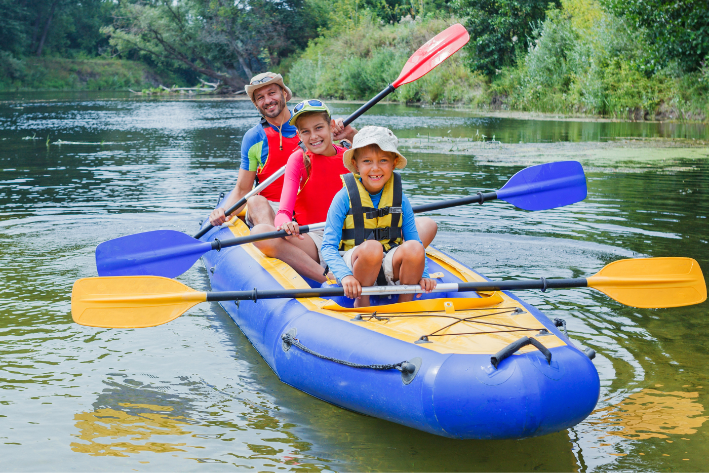 A family of four paddles a kayak together on a calm lake, enjoying a sunny day outdoors.