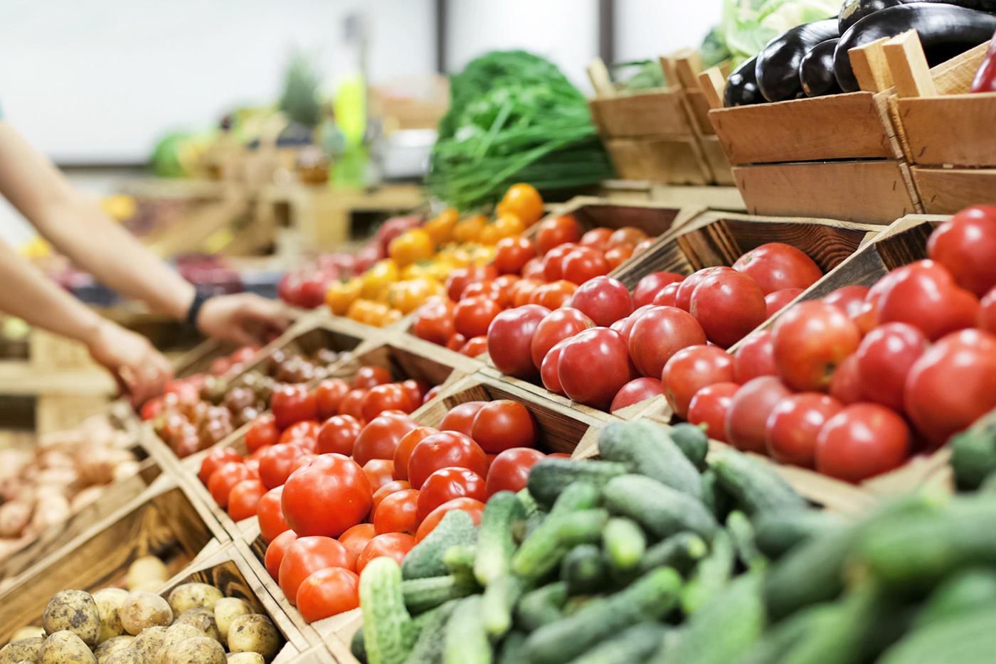 Someone's hands are seen as they browse boxes of fresh produce at a local farmers market.