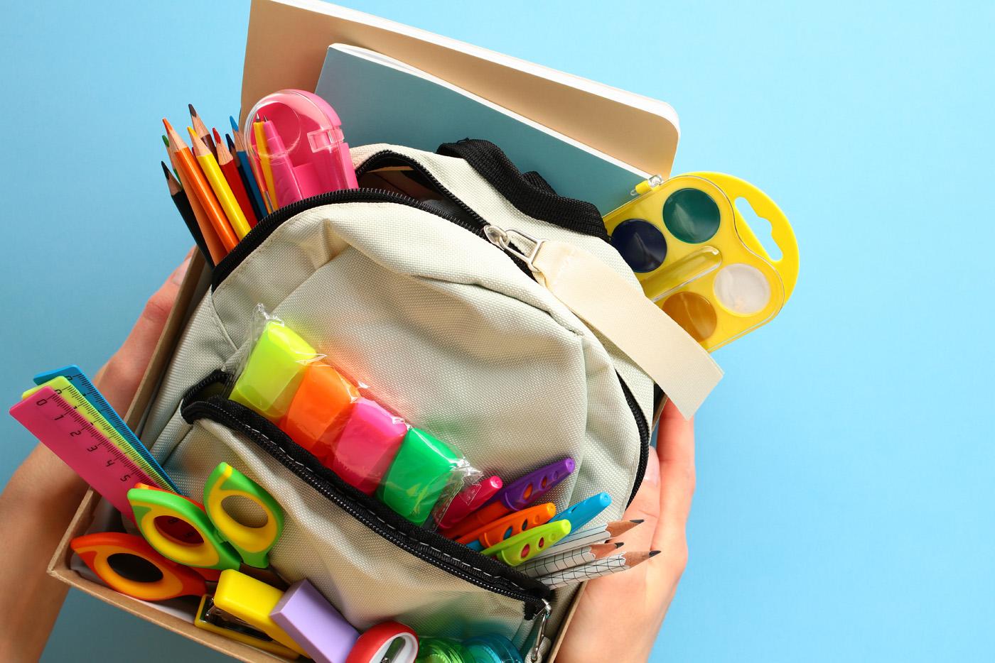 A box of assorted school supplies including markers, pencils, notebooks, and backpack.