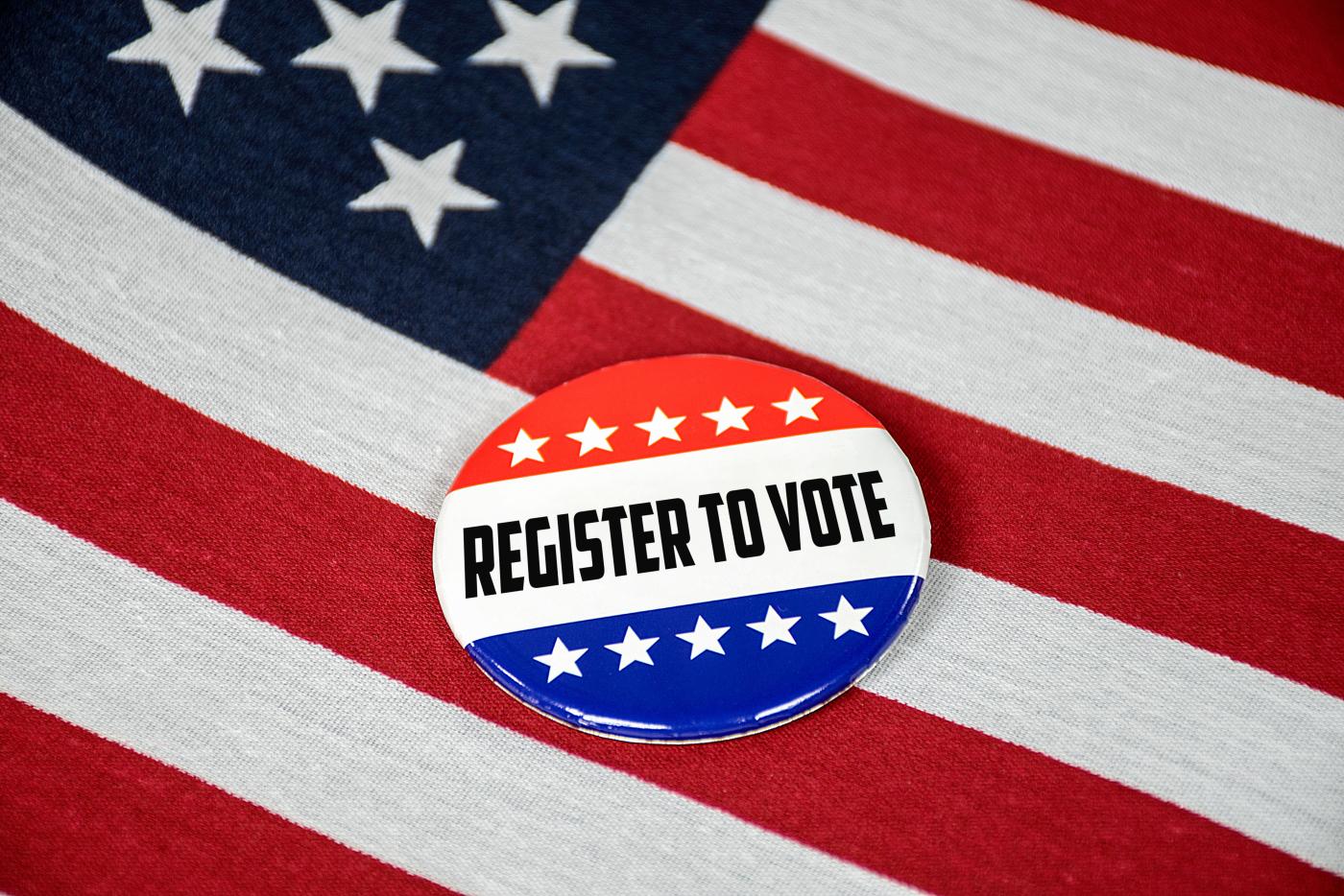Round badge with red, white, and blue colors reading 'Register to Vote' placed on an American flag.
