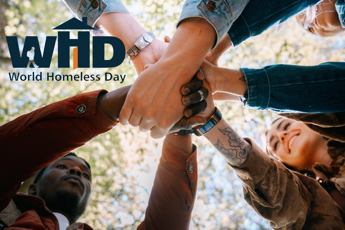 Group of people joining hands in unity outdoors under sunlight for World Homeless Day
