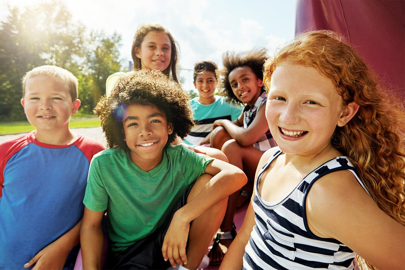 A diverse group of smiling middle school kids outside together on a sunny day.