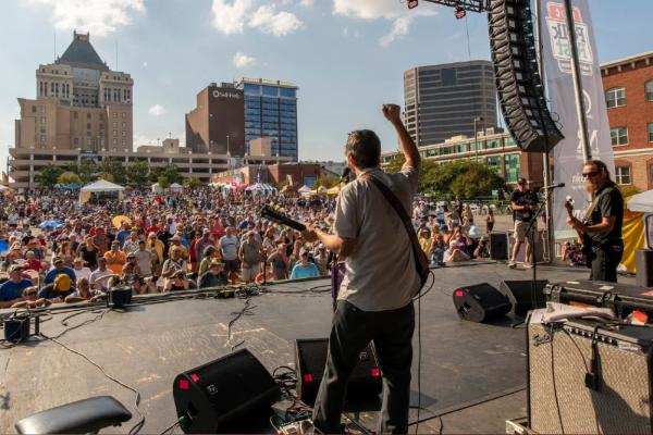View from stage of band performing to a crowd outside in downtown Greensboro North Carolina during the annual Folk Festival on a sunny day.