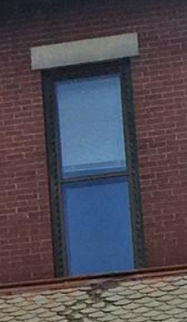 A wood window painted green with two panes of glass and a stone lentil surrounded by a brick wall