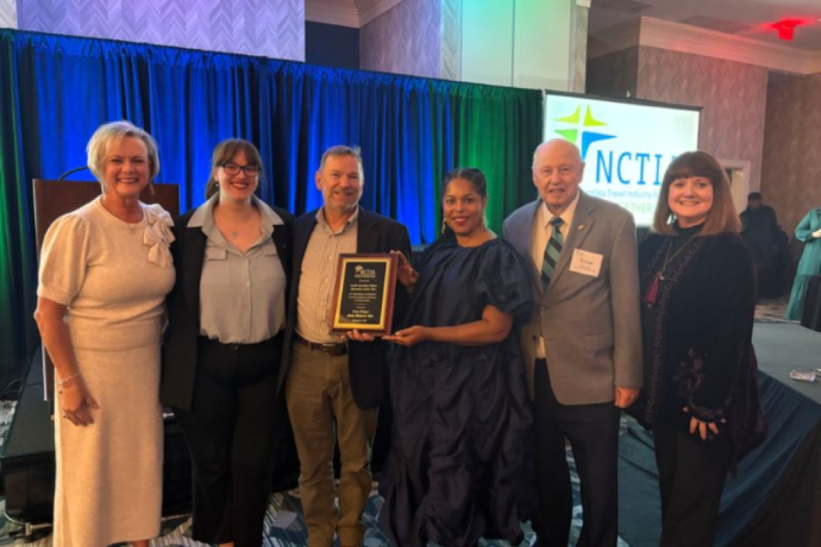A group of six people pose together, holding an award plaque