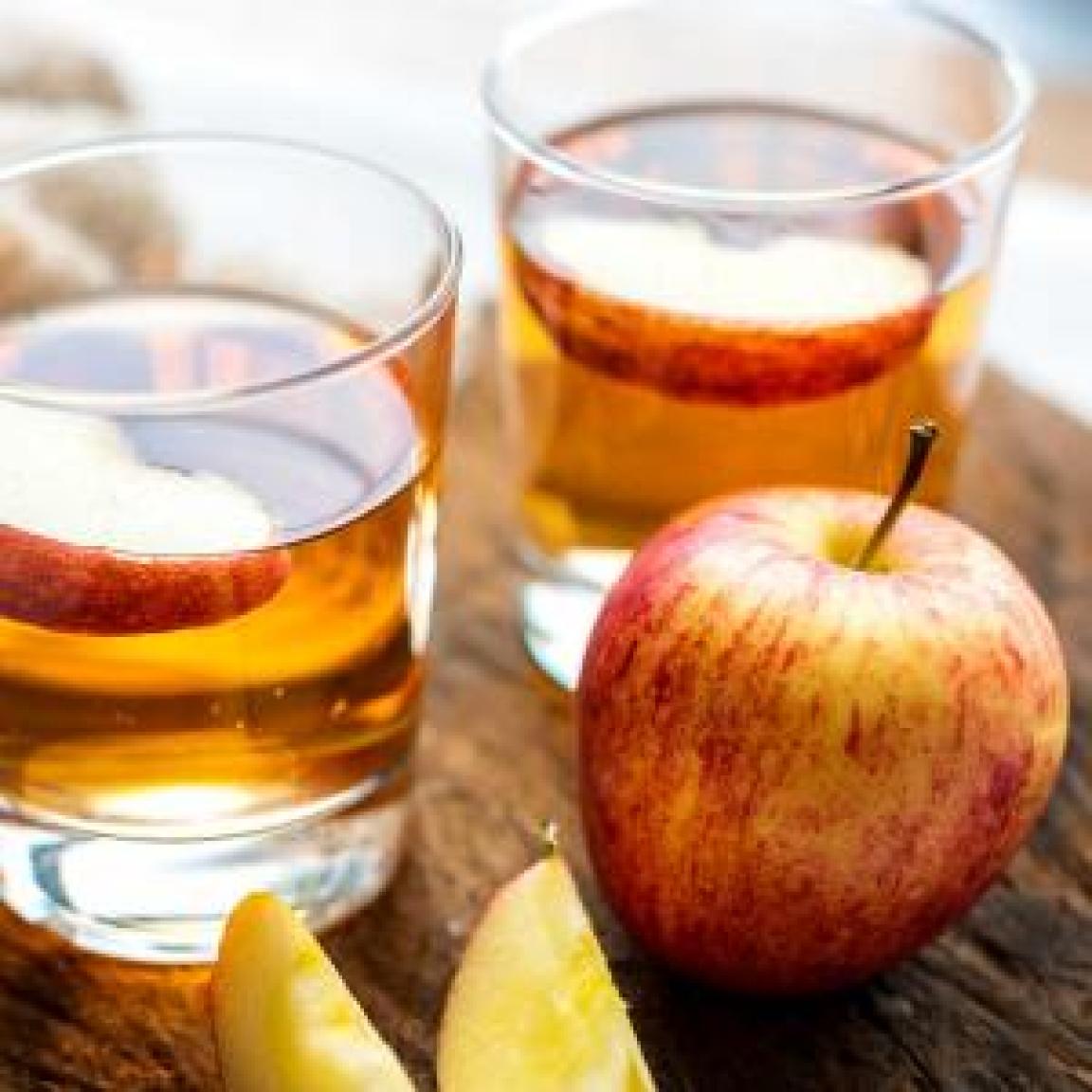 Two glasses of apple juice and a fresh apple on a table