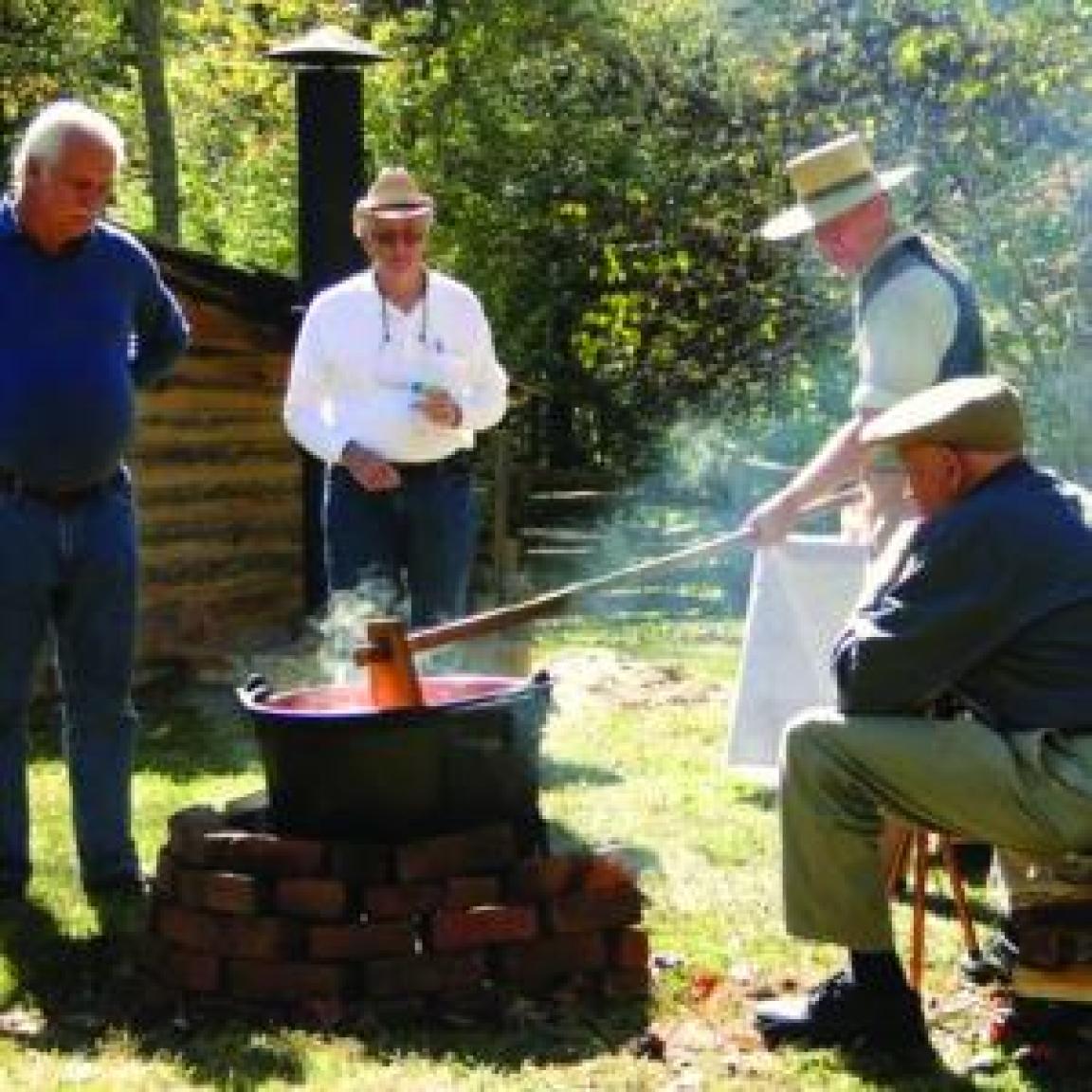 Man stirring apple butter in a cauldron with people watching