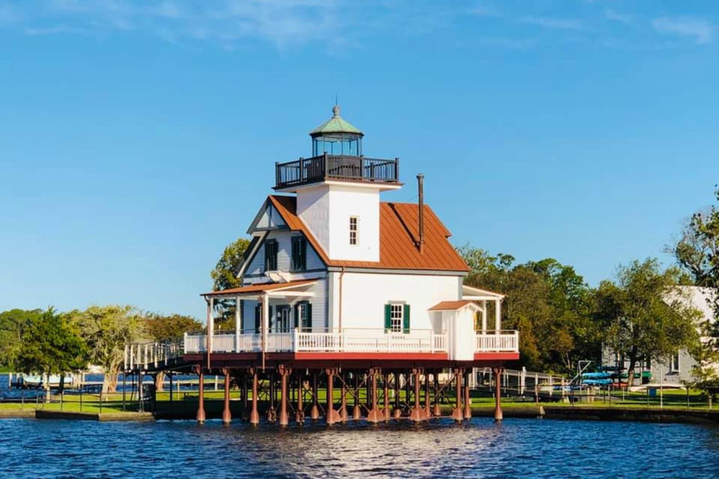 A two story house with a lighthouse tower rising a little taller on piers in the water