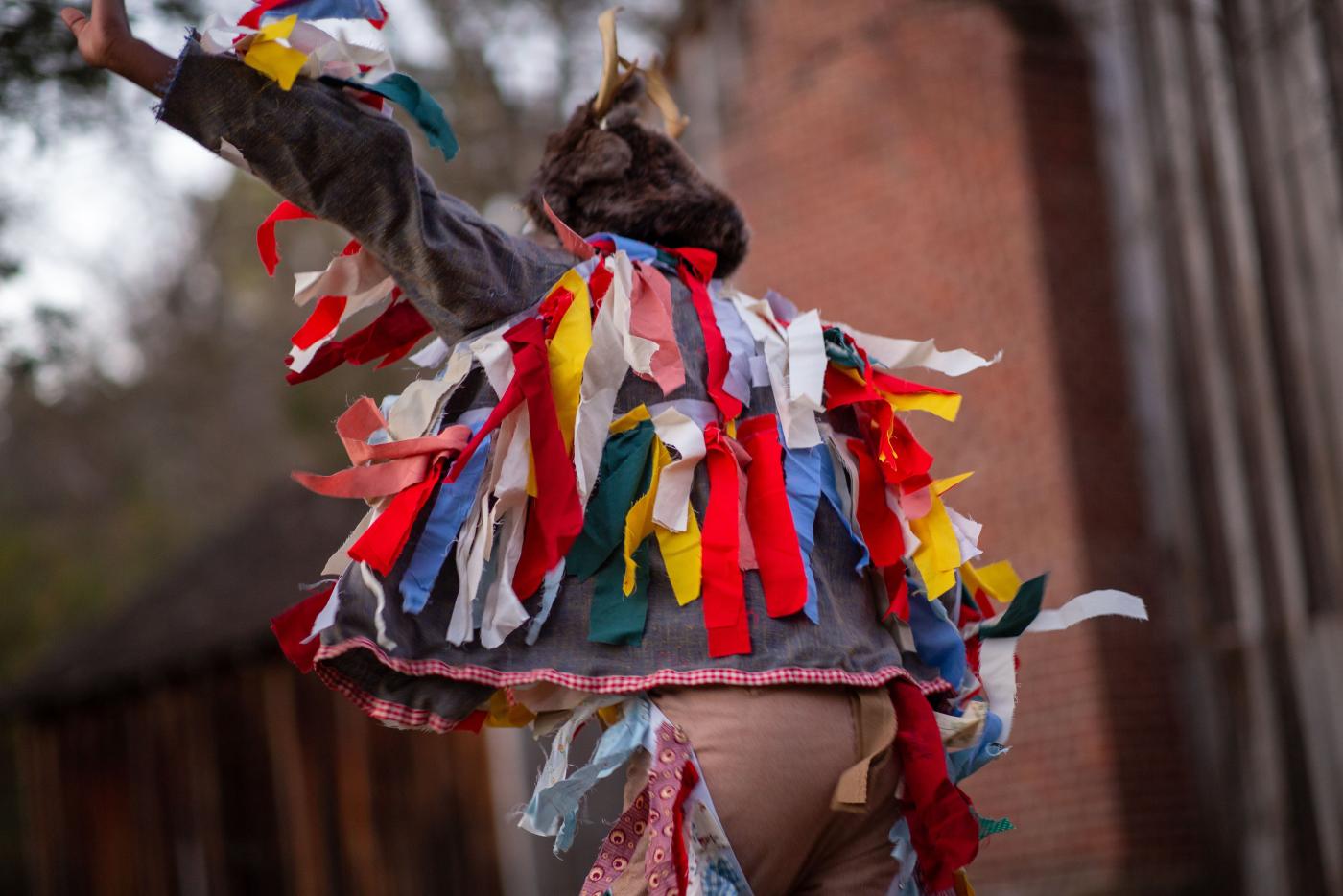 a dancer moves his arms dressed in a masquerade costume of many colors