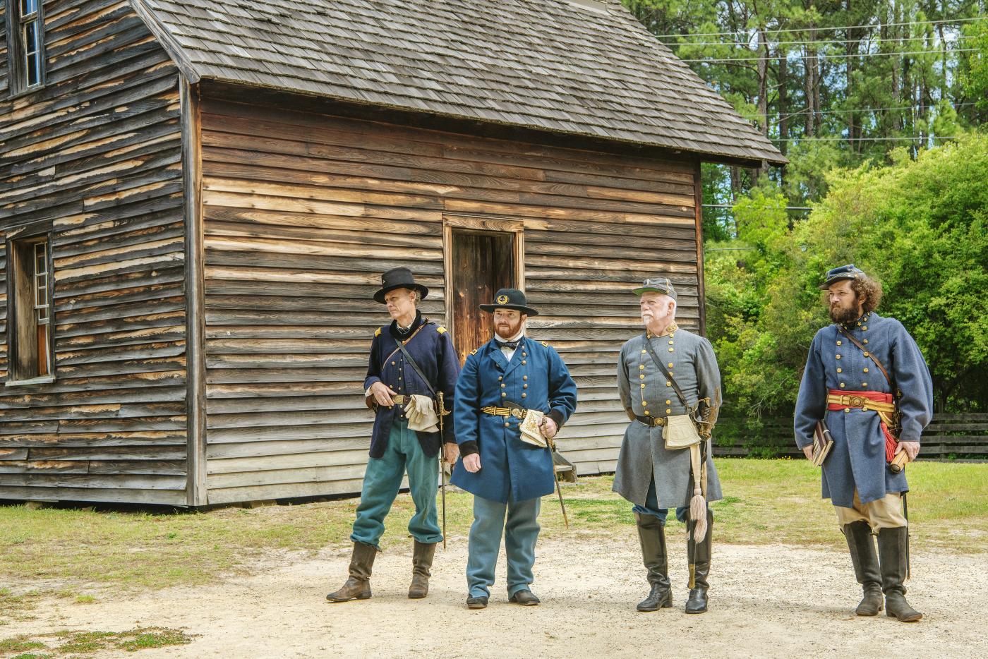 Four men dressed as Civil War generals stand outside a 19th century wood home