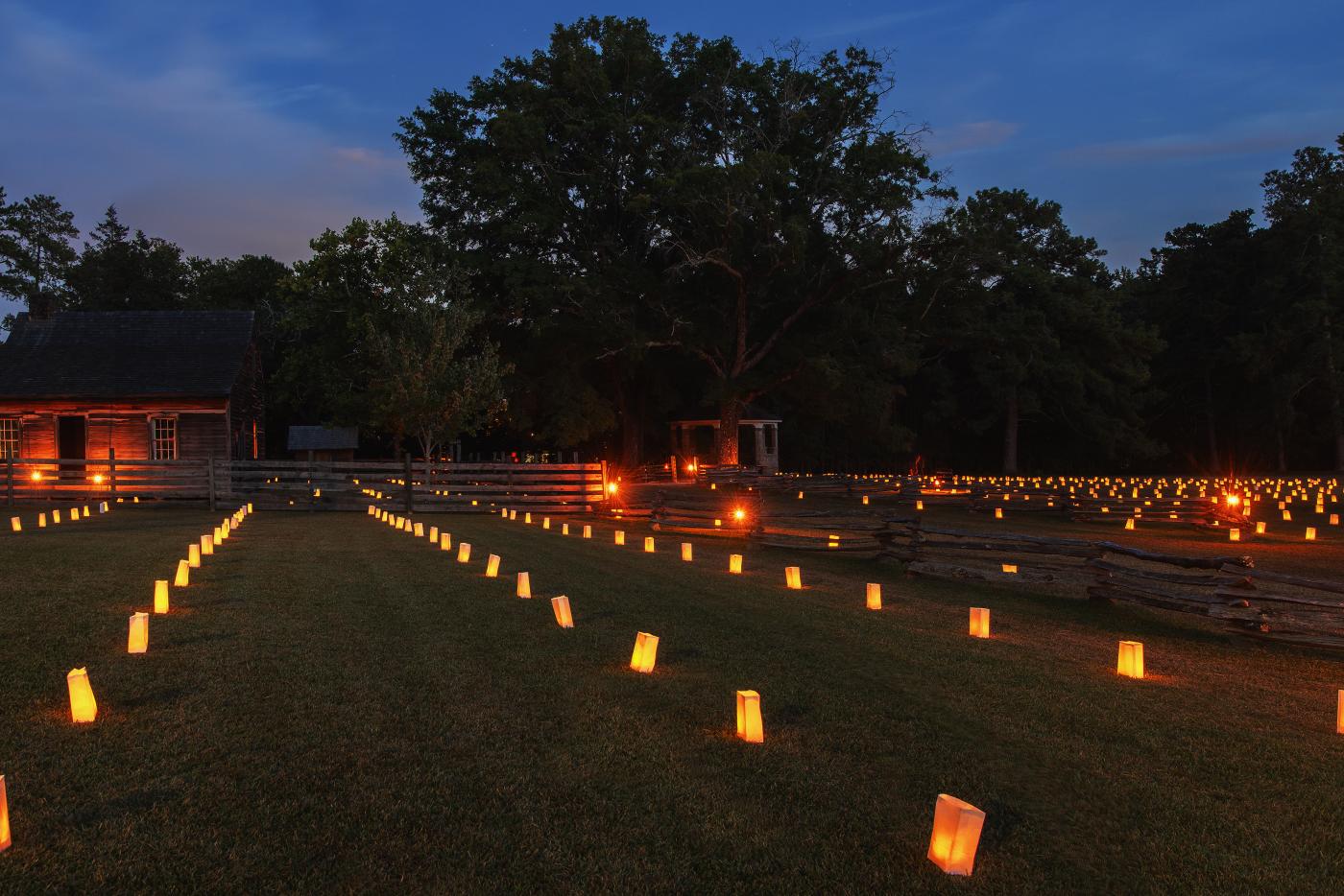 Luminaries across an open field with 19th century wood house in the background