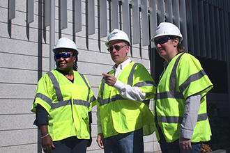 Three people in construction vests and hard hats looking in the same direction Three people in construction vests and hard hats looking in the same direction