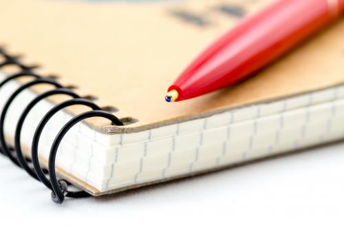 A spiral notebook with a red pen on top of it A spiral notebook with a red pen on top of it