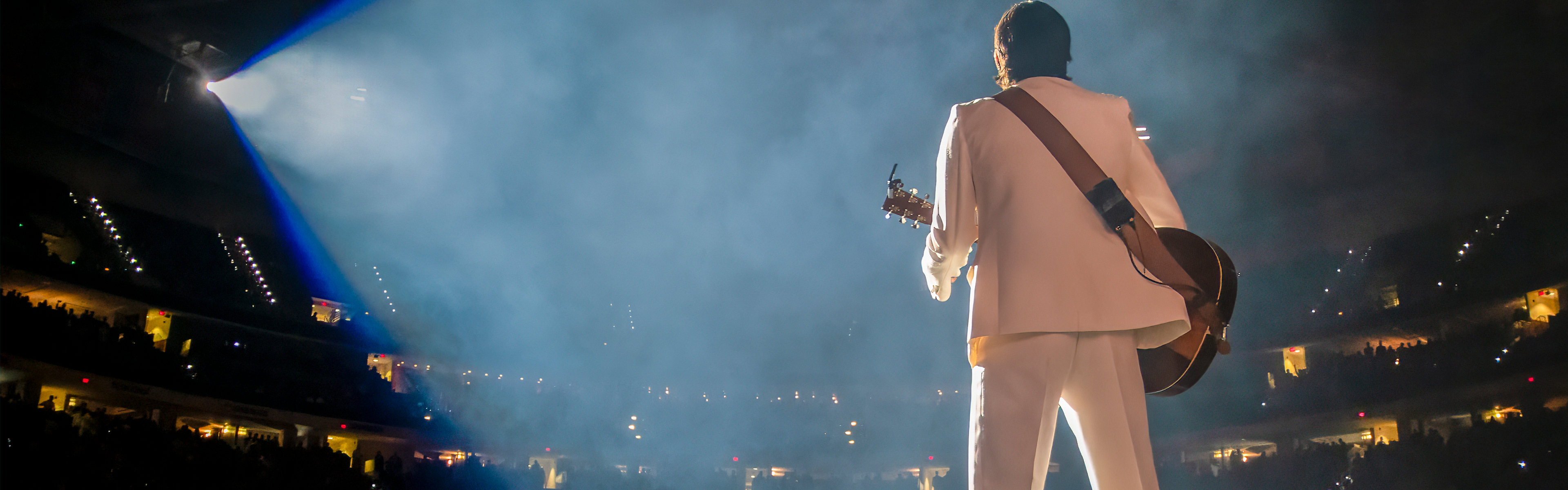 Guitarist on stage at a stadium in front of hundreds of fans.
