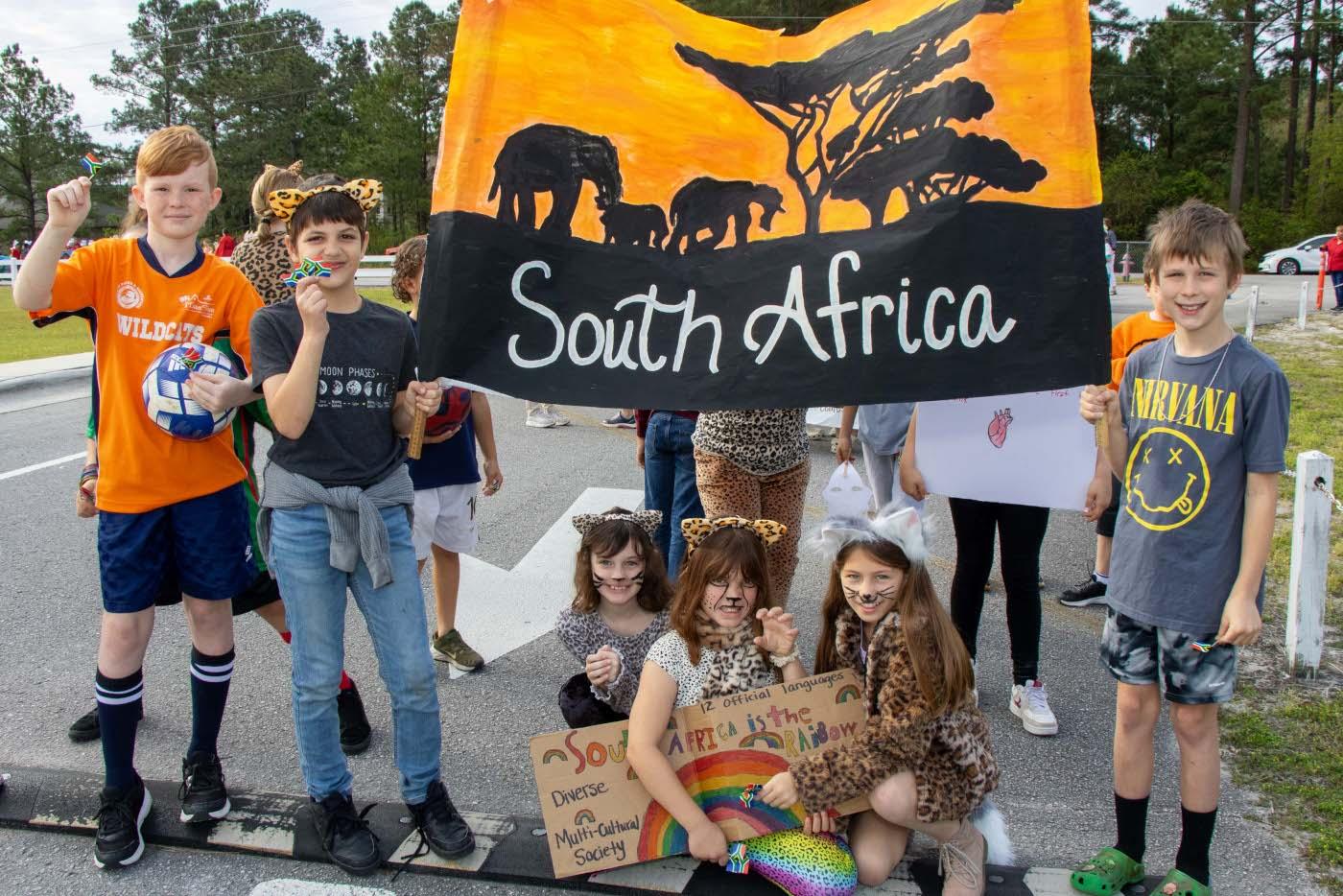 Elementary School students pose with a flag they painted with elephants, trees and the words “South Africa.”