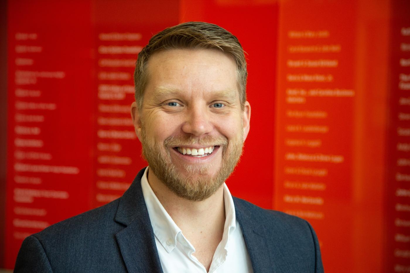 A headshot of Shaun Kellogg in front of a red background.