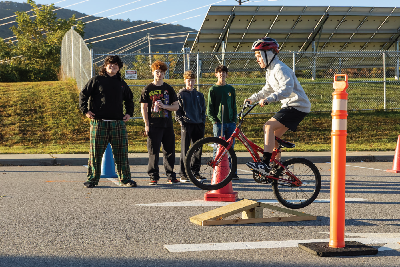 A middle school student riding a bike up a small ramp as classmates look on.
