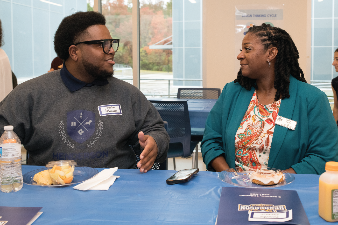 Tamika Farmer and a student sit at a cafeteria table talking at Henderson Collegiate.