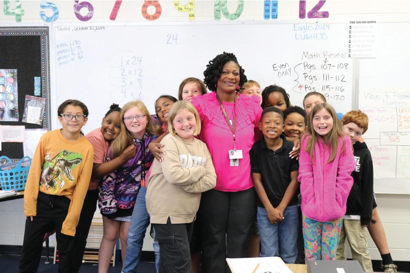 A teacher poses in front of a whiteboard with a group of elementary school students.