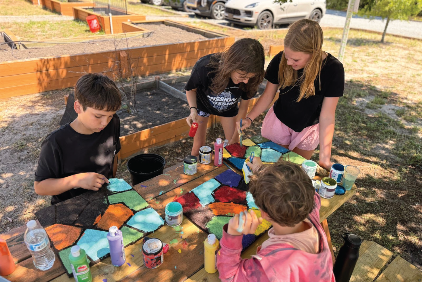 Four students paint on an outside picnic table.